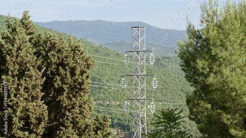 High-voltage power transmission tower with multiple insulators and electric cables stretching across a misty mountainous landscape. Multiple shots.