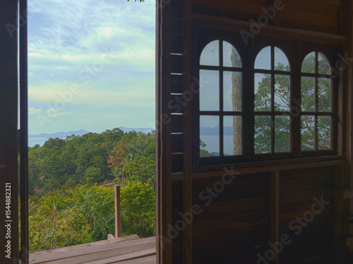 Wooden Window Frame with Arched Glass and Wide View of Forested Hills and Ocean Under Bright Sky
