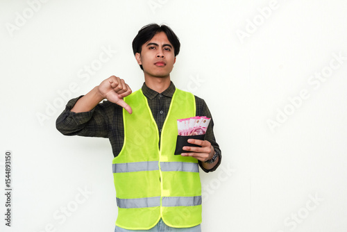 Asian construction worker seriously shows thumbs down while holding a wallet. A powerful visual representing financial struggle or disapproval