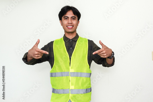 Portrait of a smiling Asian construction worker man pointing downward with friendly expression, isolated on white background, ideal for advertisement or corporate content