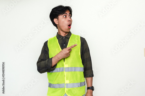 Portrait of a Asian construction worker man pointing sideways with a funny wow expression, isolated on white background for advertisement or promotional use