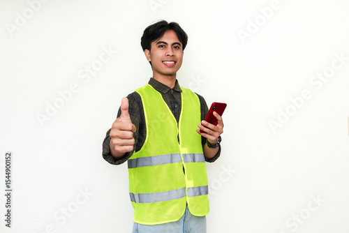 Happy Asian construction worker holding smartphone and showing thumbs up with cheerful expression, isolated on white background. Great for technology, service, or promotion themes