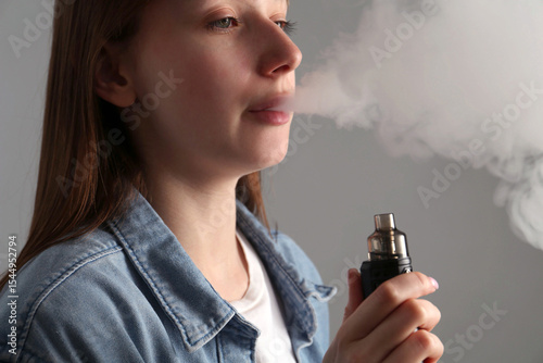 Woman using electronic smoking device on grey background