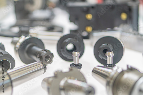 Close-up of scattered metallic mechanical parts on a light grey surface, possible industrial setting Variable shapes gears, rings, rods, sizes, and angles Overhead lighting casting soft shadows a