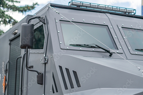 Gray armored personnel carrier APC under overcast skies, angular shape, multiple windows, tinted or protected, antenna, rugged terrain design, side perspective, no visible texts or branding, open a