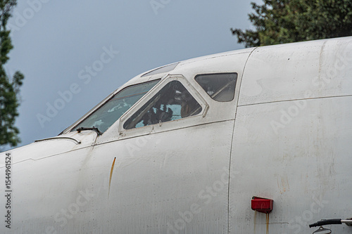 An aged white single-engine aircraft, parked outdoors on an overcast day with open cockpit windows The wing extends to the left and theres a small red anti-collision light at the tip Natural setti
