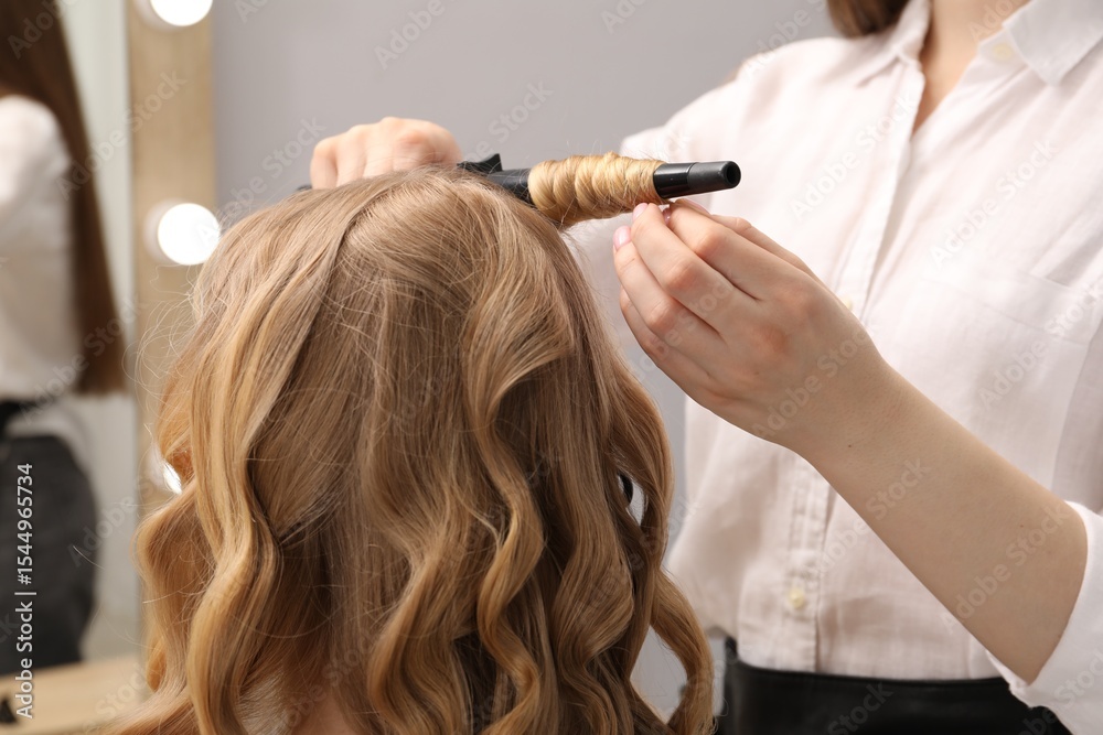 Fototapeta premium Hairdresser curling woman's hair in salon, closeup