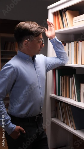 vertical video Pensive office worker choosing book from bookshelf in library