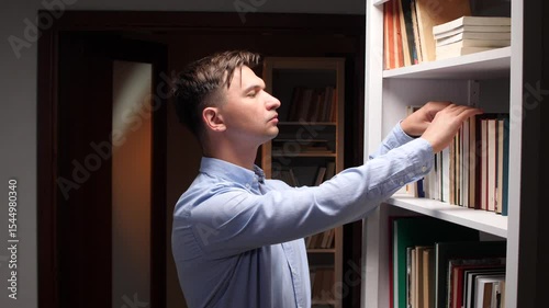 Young man searching for book in home library