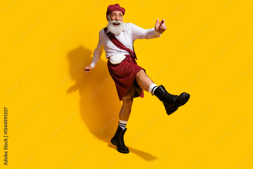 Smiling elder man in Scottish attire making joyful gestures against vibrant yellow studio backdrop Smiling elder man in Scottish attire making joyful gestures against vibrant yellow studio backdrop