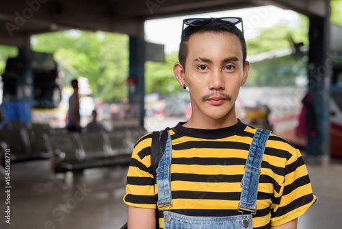 Portrait of nonbinary genderfluid young Asian gay tourist man in bus terminal