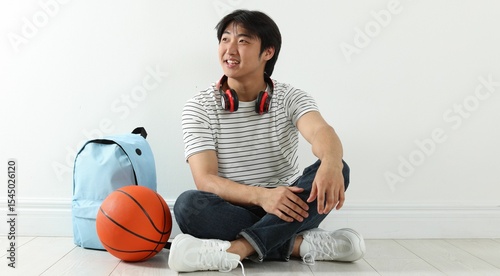 Happy student with basketball ball and backpack on floor indoors photo