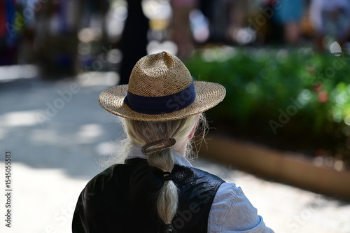 An elder man with long, grey hair tied in a braid. A man wears a straw hat. An attentive, old man in a park in Berlin-Kreuzberg.