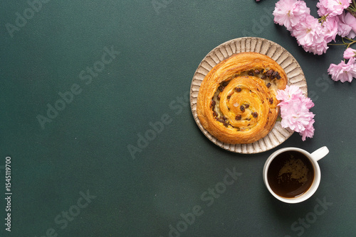 Fresh pastry and coffee with pink flowers on dark green surface background