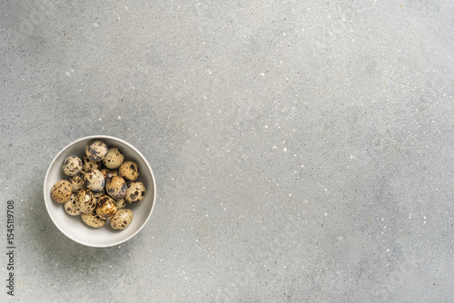 Quail eggs in white bowl on gray speckled surface minimalist design