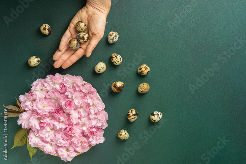 Hand holding quail eggs with pink flowers on green background