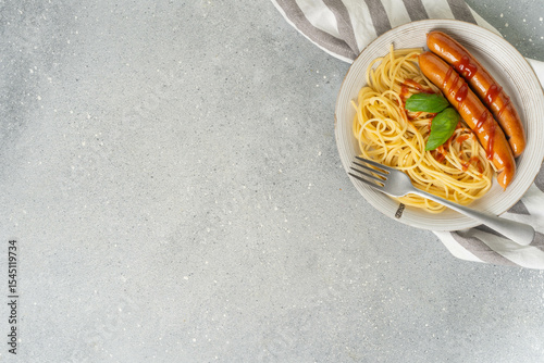 Plate of spaghetti with sausages on gray tablecloth