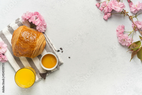 Breakfast composition with pain au chocolat and orange juice surrounded by pink cherry blossoms