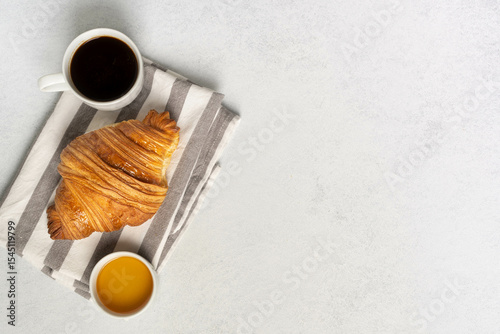 Croissant with coffee and orange juice on striped napkin on light surface