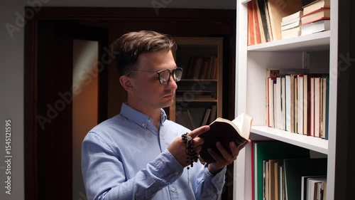 Believer reading holy book and holding rosary beads in library