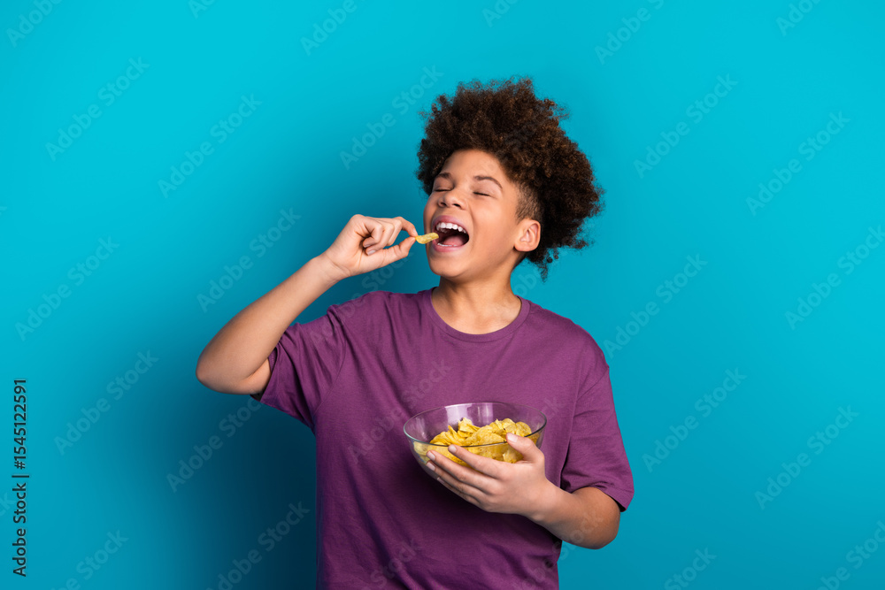 Smiling young boy in purple shirt enjoying snacks against vibrant blue background showcasing joy and leisure Smiling young boy in purple shirt enjoying snacks against vibrant blue background showcasing joy and leisure