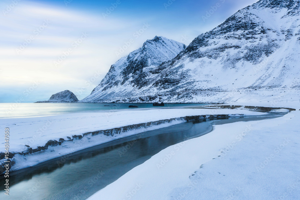 Obraz premium Beautiful snowy mountains with ice in foreground and golden sunlight at sunrise in winter in Lofoten islands, Norway. 