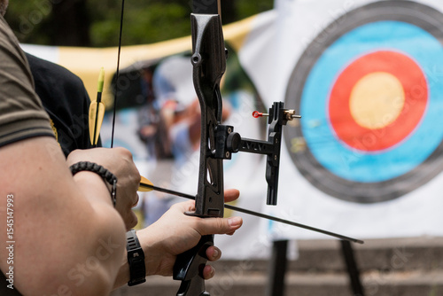 Archer Aiming Compound Bow at Target: Outdoor Archery Sport with Blue Target and Focused Male Participant, Black Equipment and Natural Light