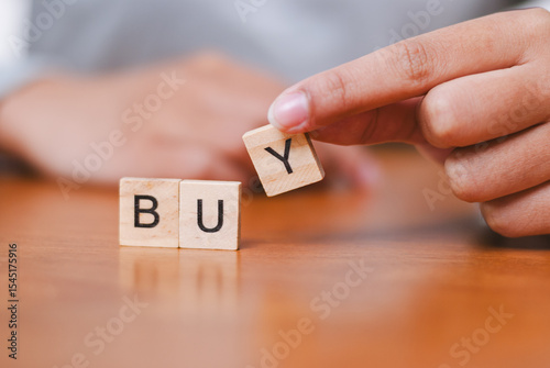 Engaging buying process action indoor table setting close-up perspective hand showcasing word 'buy' with wooden letters