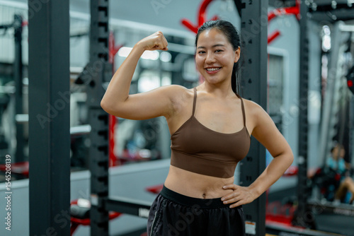 Strong asian woman flexing biceps in a gym