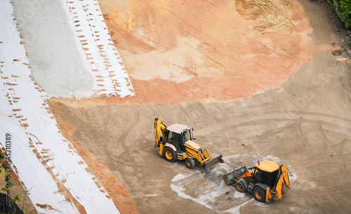 Two tractors leveling gravel at a construction site, preparing for park or infrastructure development