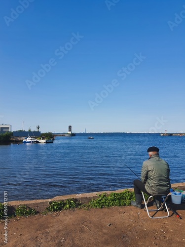 Tranquil seaside fishing scene with man sitting by water on a clear summer day