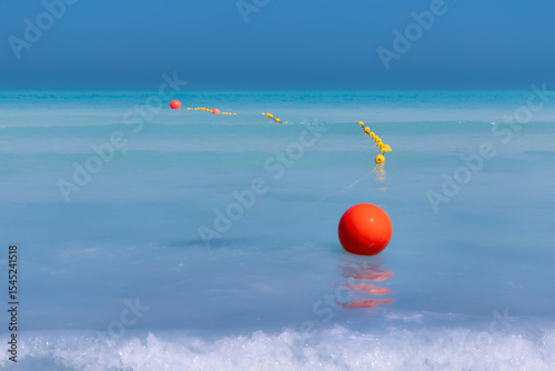 Swimming area boundary with bright yellow buoys on turquoise calm sea water on sunny day