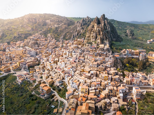 Town with many houses on hillside and rocky cliff on sunny day, Gagliano Castelferrato, Sicily, Italy