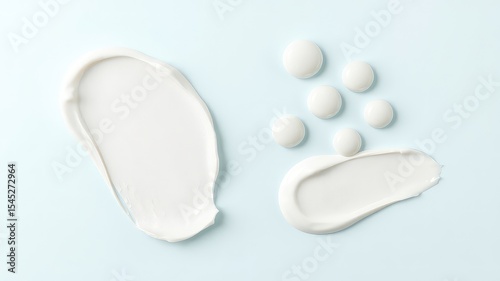 Smooth swirls and neat round blobs of creamy white beauty product arranged artistically on a soft light blue backdrop