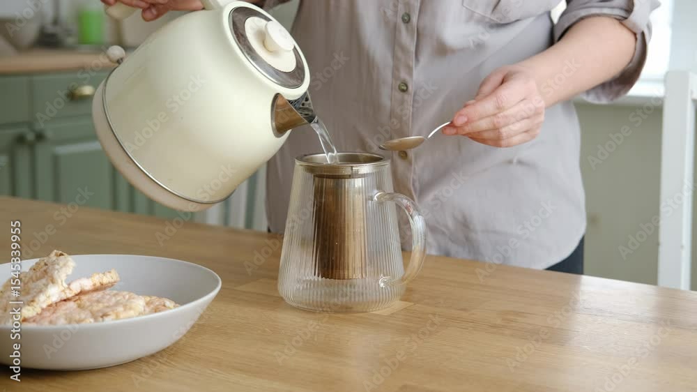 Woman making tea. Female pouring a hot water to Glass teapot with black tea. Drinking hot tea, healthy freshly brewed detox drink. Preparing herbal tea in kitchen. Morning routine.