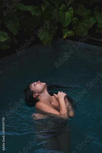 A woman with braids enjoying in a pool, surrounded by lush tropical leaves in a serene and intimate moment in Ubud, Bali, Indonesia