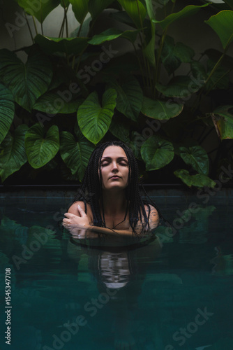 A woman with braids enjoying in a pool, surrounded by lush tropical leaves in a serene and intimate moment in Ubud, Bali, Indonesia