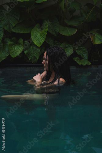 A woman with braids enjoying in a pool, surrounded by lush tropical leaves in a serene and intimate moment in Ubud, Bali, Indonesia