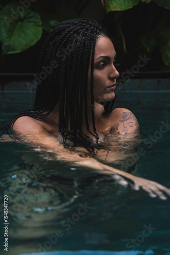 A woman with braids enjoying in a pool, surrounded by lush tropical leaves in a serene and intimate moment in Ubud, Bali, Indonesia