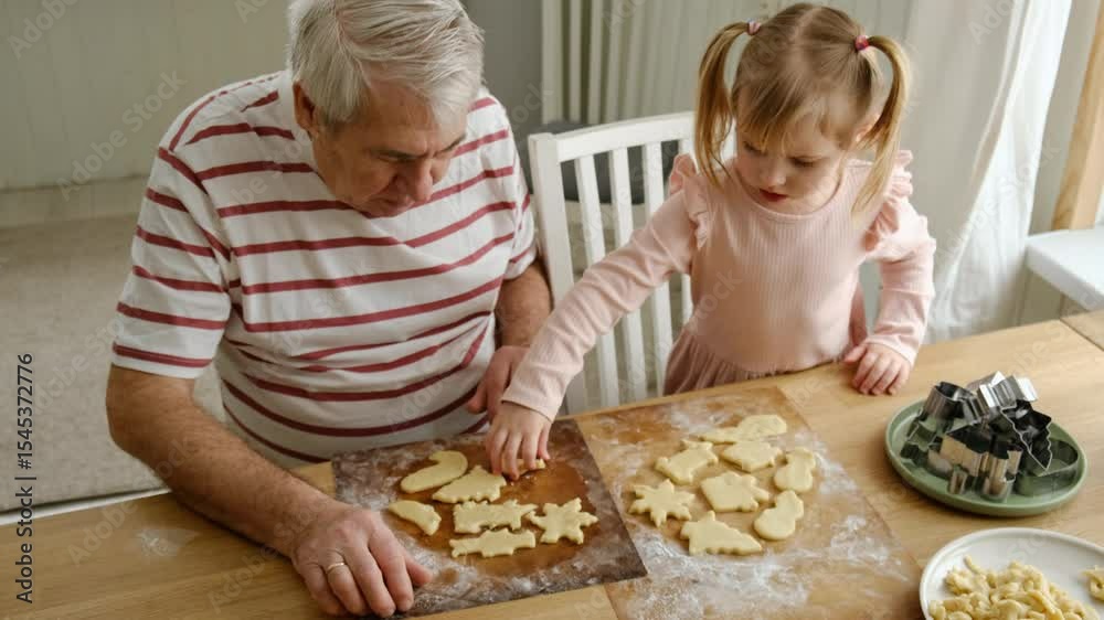 Grandfather and little grandchild baking, cooking and making homemade cookies or biscuits together in a home kitchen. Cute child girl helping elderly senior man, bonding and learning how to bake.