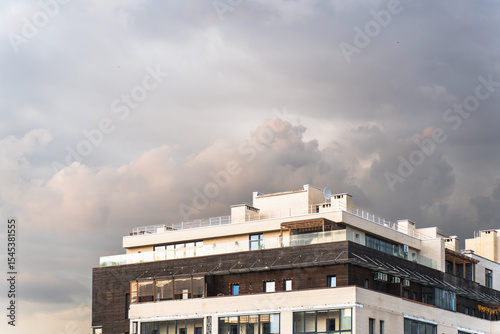 Modern residential building with a mix of brick and wood facade under dramatic evening clouds, highlighting contemporary urban architecture and weather contrast.