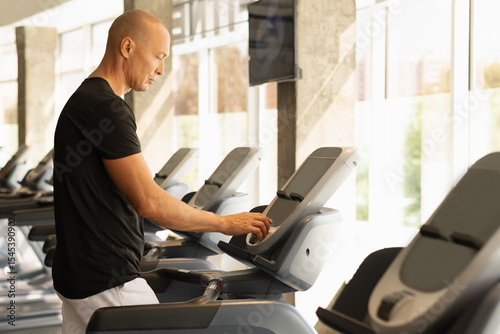 Sporty caucasian man walking on running track, warming up on gym treadmill. Running at gym. Close up.