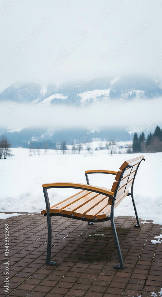 Naklejka premium Wooden park bench overlooking snow-covered landscape and foggy mountains