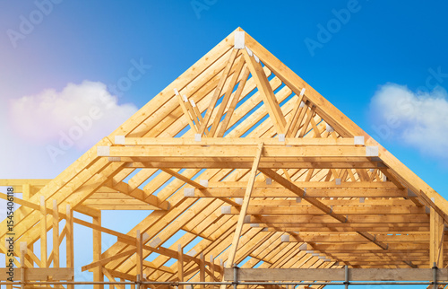 Building construction of house - Timber framing stage of a new residential home attic construction using trusses for roof structure. A construction site set against a clear blue sky.