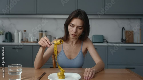 Skinny thin woman eating measuring tape demonstratively at home kitchen