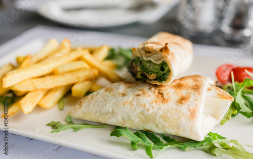 Foto Fresh tortilla wrap served with golden fries and arugula on a white plate close-up