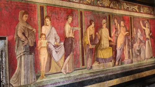 Pompeii, Italy - 8 January 2025. A fresco from the Villa of the Mysteries features a sequence of figures in ceremonial poses, likely part of an initiation scene, set against vivid red and green panels