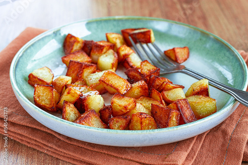 Golden crispy baked potatoes, on a green plate with a fork on a wooden table, no people