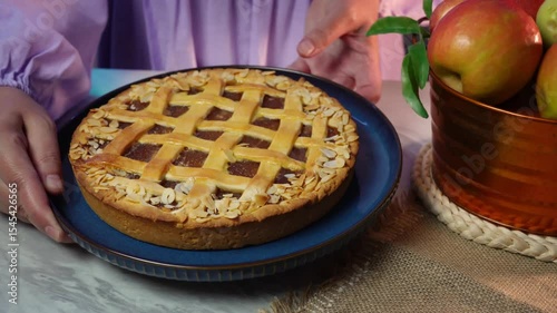 Woman presenting freshly baked apple pie with basket of apples on rustic table setting
