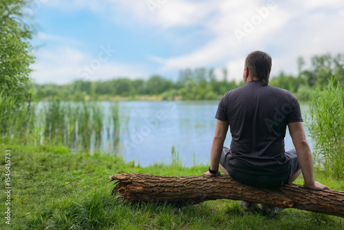 Cuadro en lienzo Young man sitting by lake in nature, seen from behind, relaxing in solitude